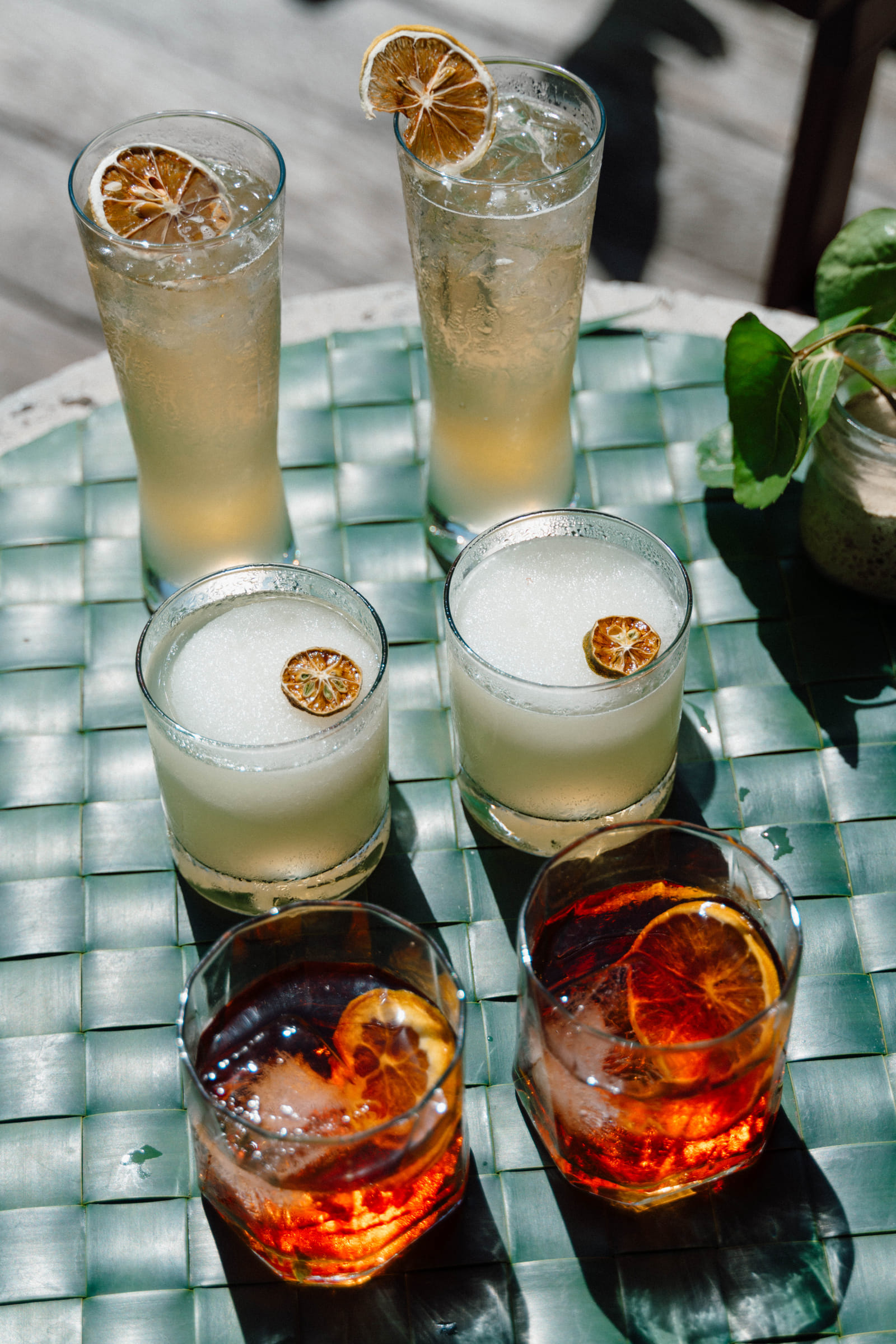 Six craft cocktails in highball and rocks glasses garnished with dried citrus wheels, served on a woven table at Bravo Beach Resort Siargao