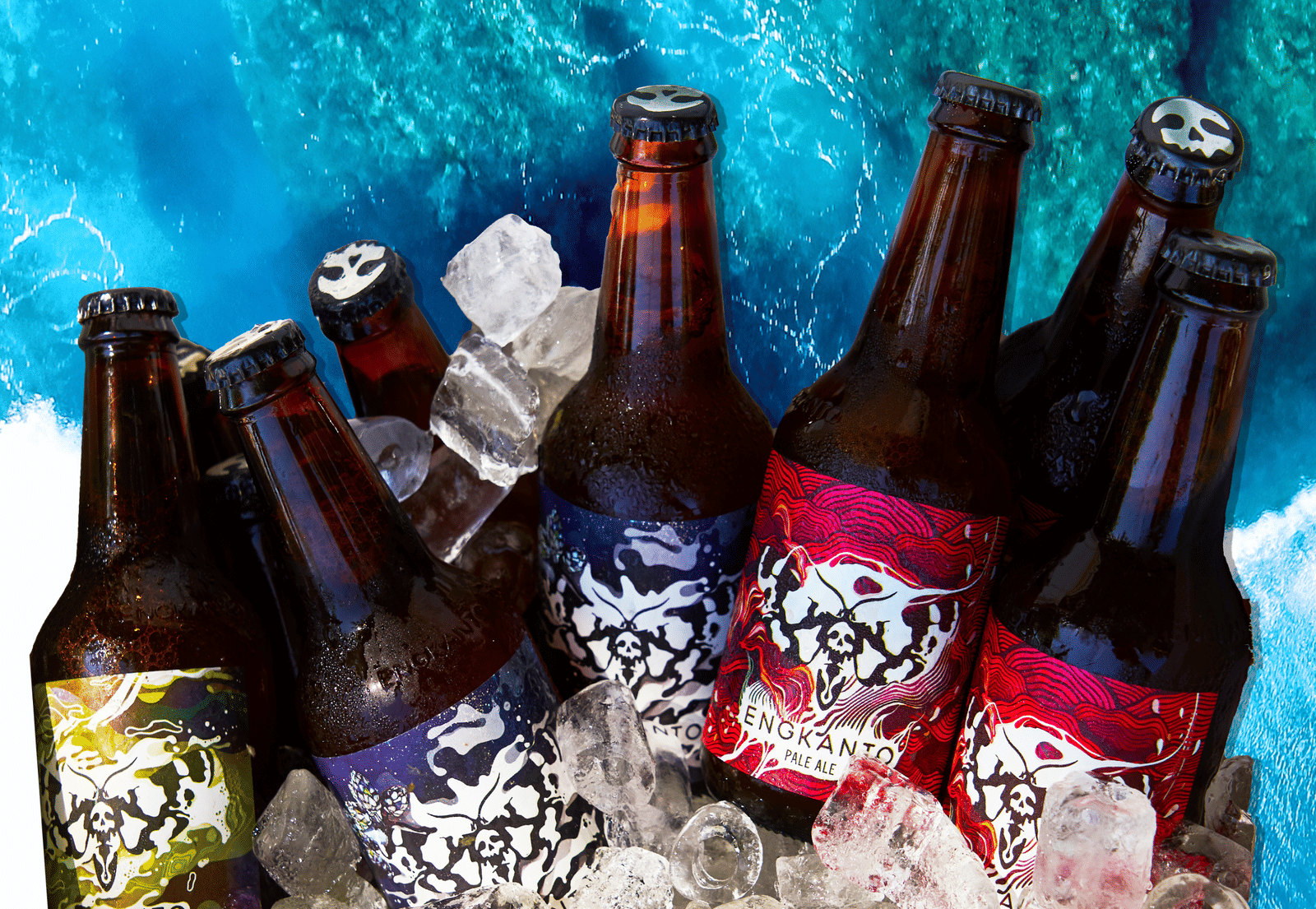Assorted bottles of Engkanto craft beer with skull-themed labels nestled in crushed ice, set against a vivid blue ocean wave backdrop