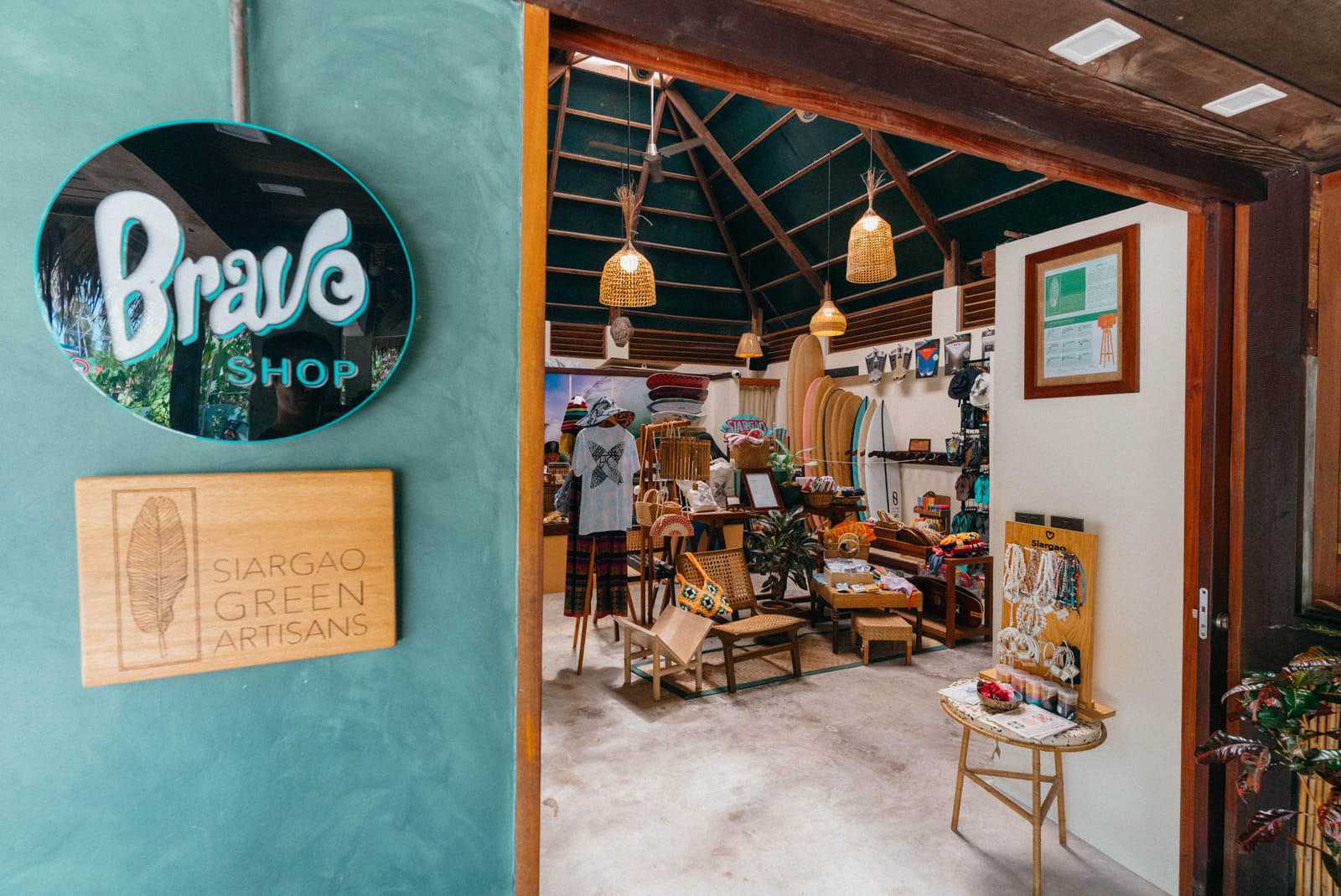 Bravo Shop sign and Siargao Green Artisans plaque on a teal wall beside the entrance to the Bravo Beach Resort Siargao shop interior