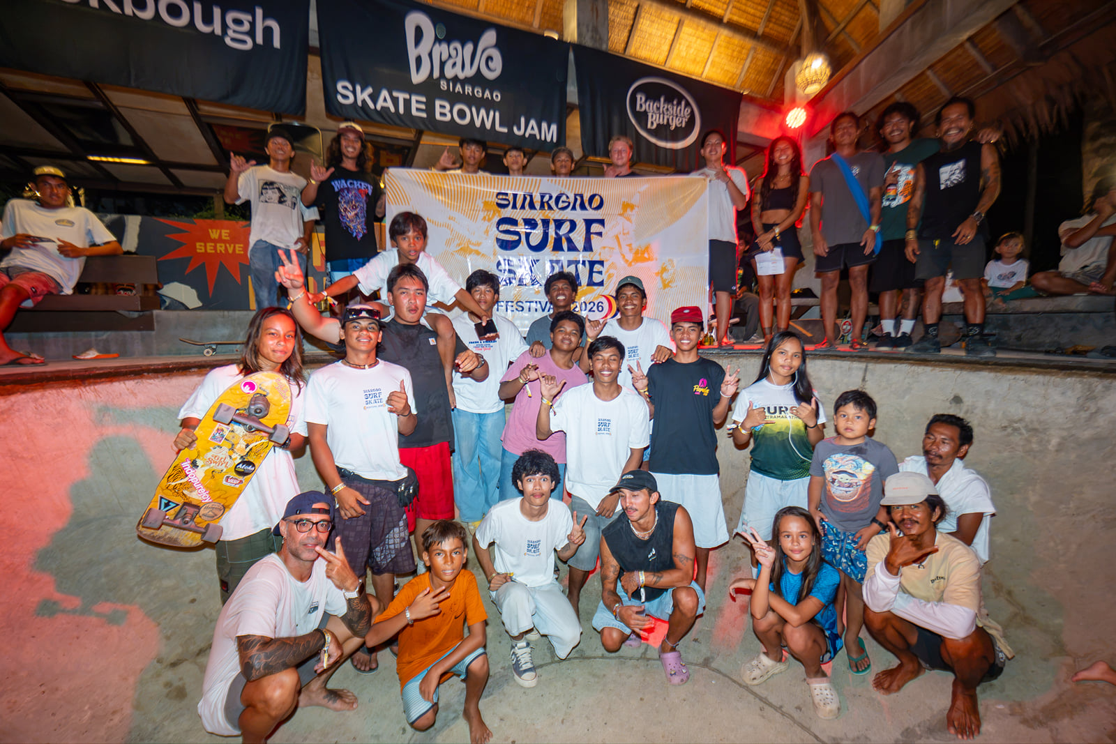 Skaters and surfers of all ages pose together in the Bravo Skate Bowl beneath a Siargao Surf and Skate Festival 2026 banner and a Bravo Skate Bowl Jam sign