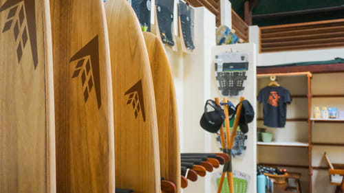 Wooden surfboards with an arrow logo displayed on racks inside the Bravo Beach Resort Siargao shop, alongside caps, fins, and branded shirts