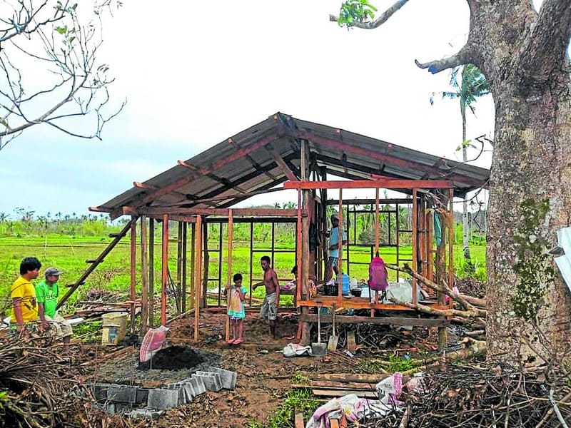 Family members and workers construct a metal-framed house on a rural plot of land in Siargao, part of a community post-typhoon rebuilding effort
