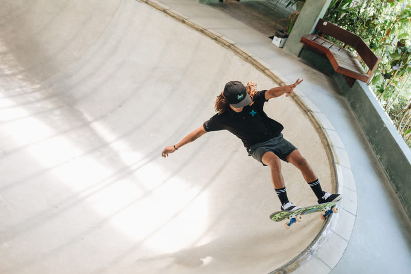 A man wearing a cap and Bravo Beach Resort Siargao branded apparel skateboards up the curved concrete wall of the resort skate bowl