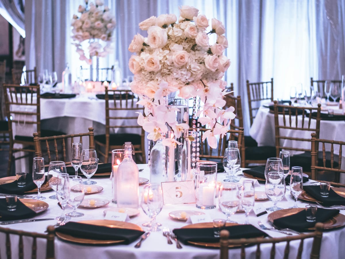 A round table laid with white linen, place settings and a floral centrepiece for a celebration