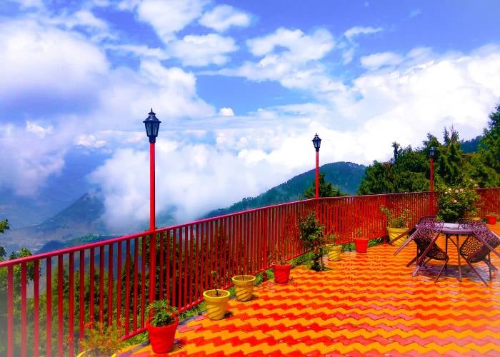 The terrace at Hotel Himdhara with red railings, lamp posts, and clouds over the hills