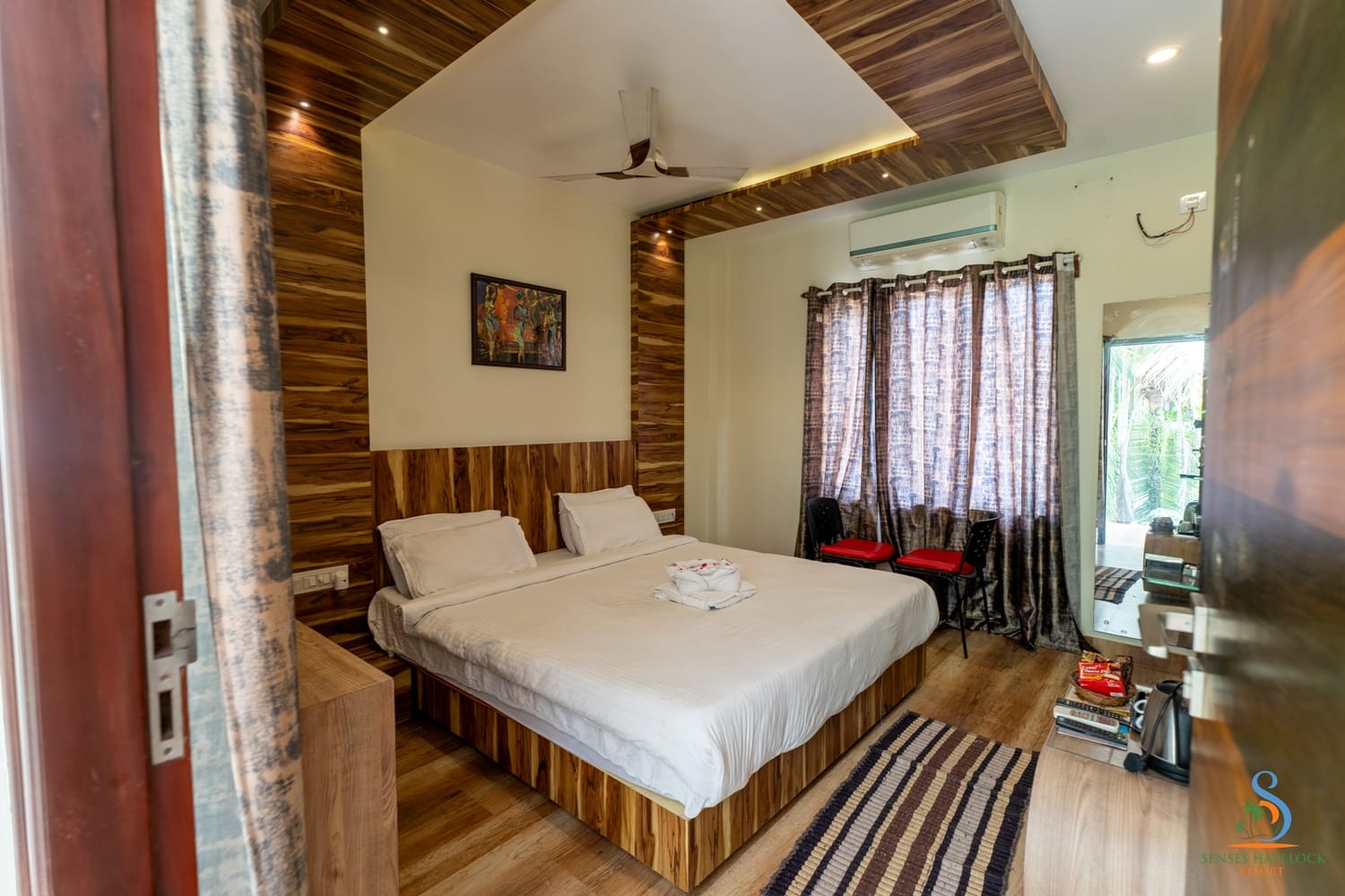 A Deluxe Room with a king bed, timber panelling and a glass door onto the coconut grove