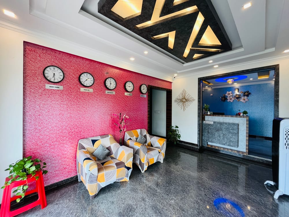 Lobby seating at Value Inn, Bangalore Airport with a patterned sofa, world clocks on a red feature wall, and the reception counter behind