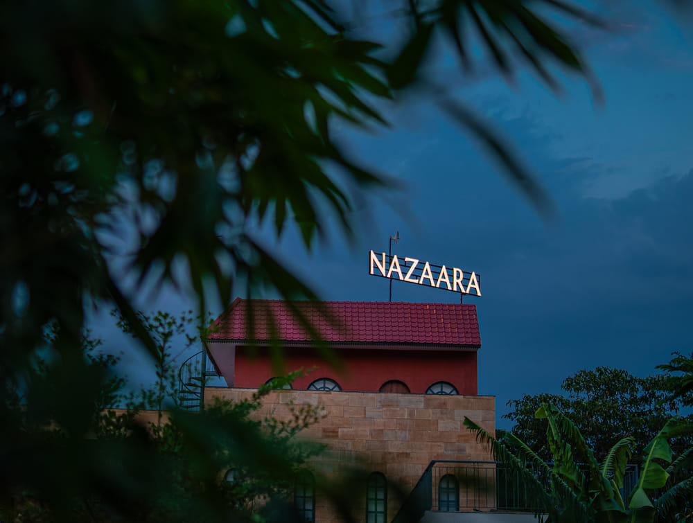 Nazaara Hills Retreat's rooftop signage and terracotta roofs, framed by tree branches against the Udaipur hills.