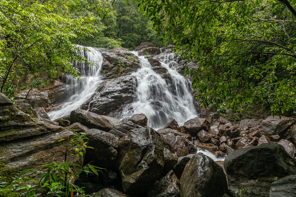A seasonal waterfall tumbling over dark rocks through green forest, a short drive from The Garud Forest, Tadoba