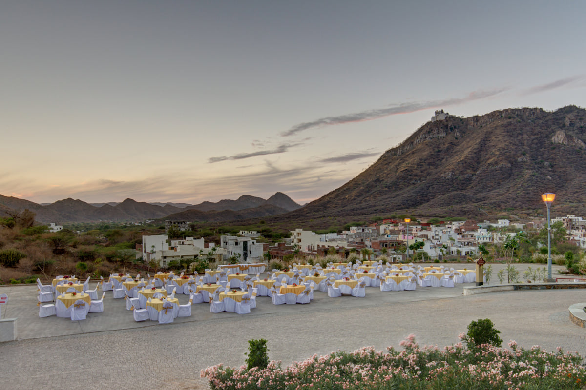 Open-air terrace set with round tables at dusk at Ramada by Wyndham Udaipur Resort and Spa