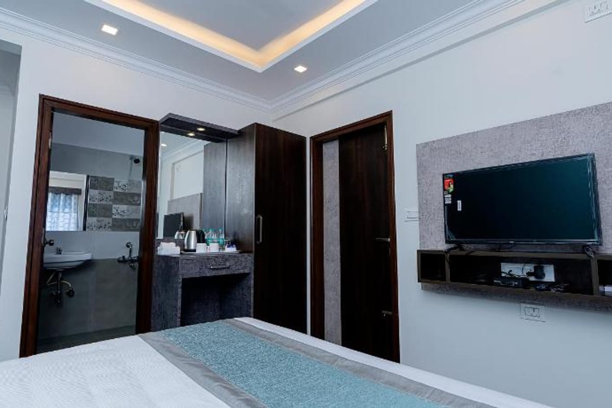 Wall mounted TV, dressing mirror, and bathroom entrance in the Standard AC Room at Value Inn, Bangalore Airport with dark wood doors