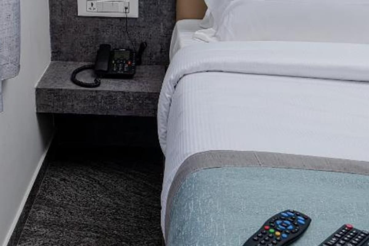 Bedside detail in the Standard Non-AC Room at Value Inn, Bangalore Airport with a telephone, TV remotes, and a stone finish side shelf