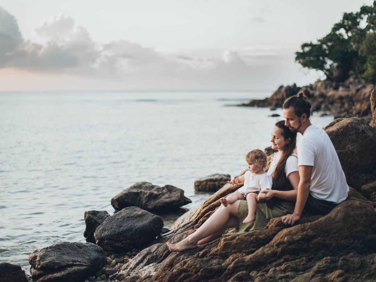 A family sitting together on the rocks at dusk, looking out over calm water