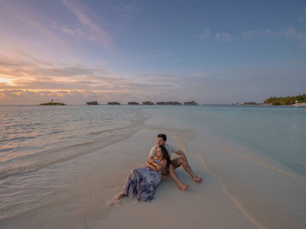 A couple resting on a sandbar at sunset, the shallows running out towards the horizon