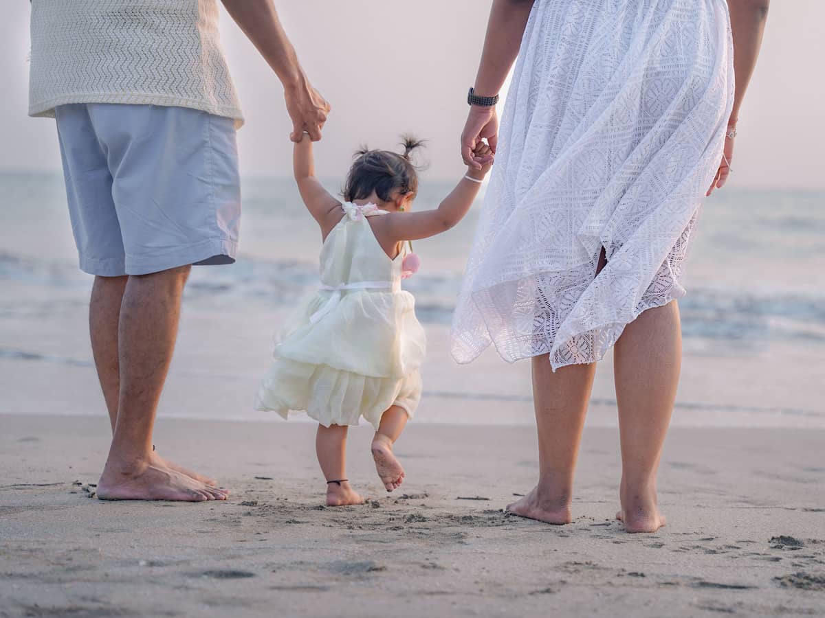 Parents walking hand in hand with a small child along the wet sand