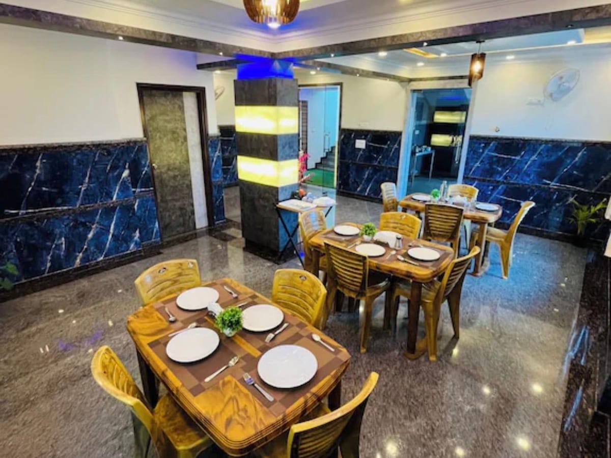 Tables laid for a meal in the dining area at Value Inn, Bangalore Airport with marble walls, pendant lights, and a blue lit ceiling design