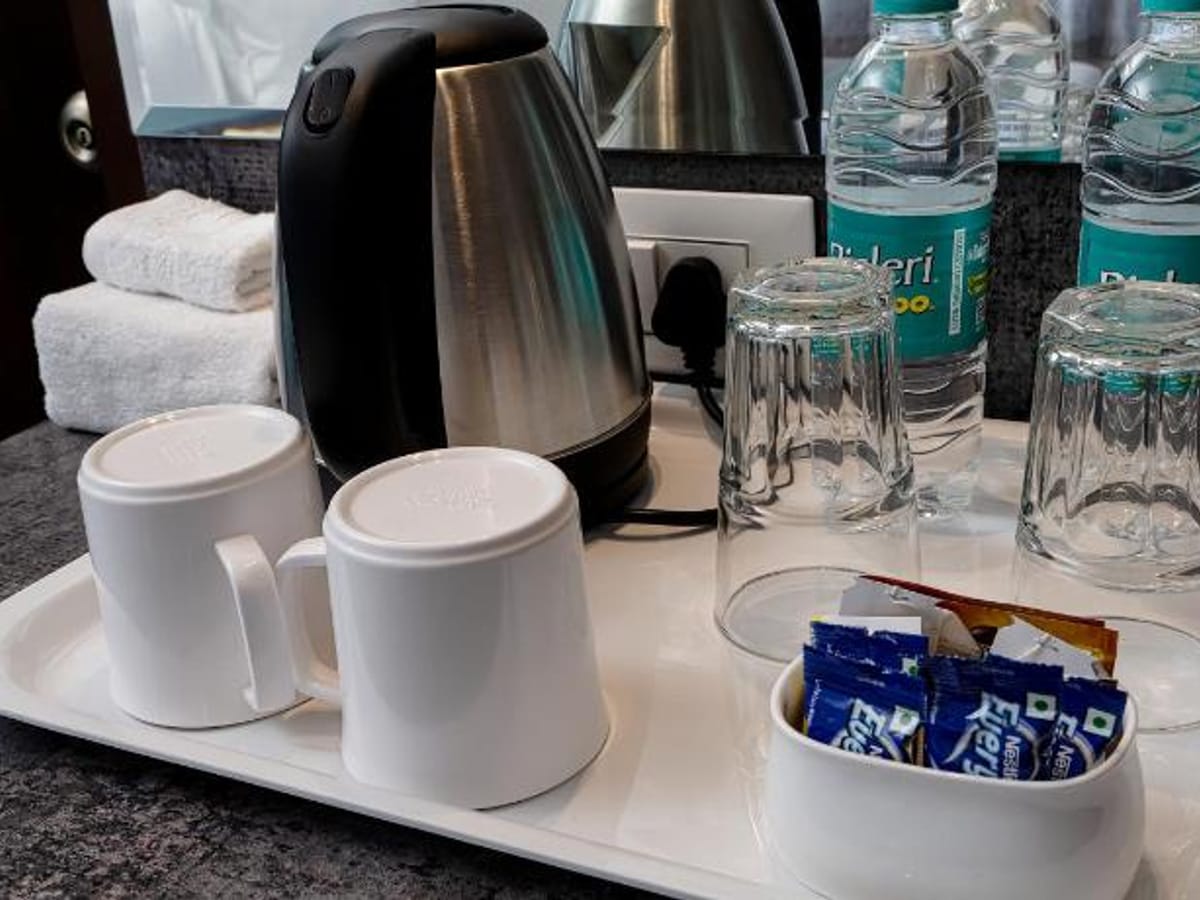 Tea and coffee tray at Value Inn, Bangalore Airport with an electric kettle, cups, glasses, biscuit sachets, and bottles of mineral water