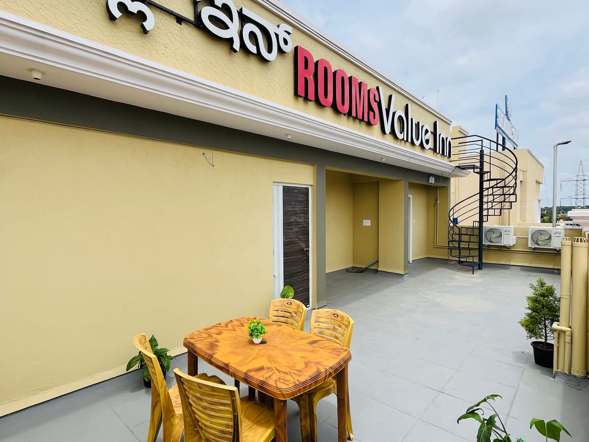 Wooden dining table and chairs on the rooftop terrace at Value Inn, Bangalore Airport beside the hotel signage and potted green plants