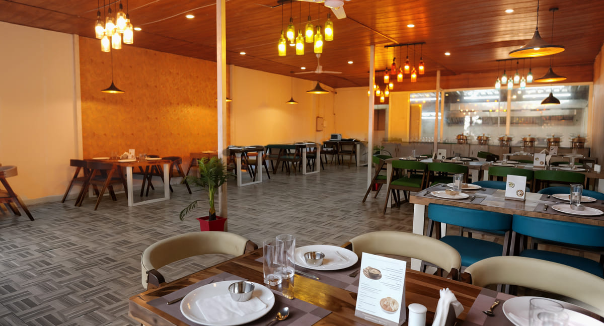 Fine Dine restaurant dining hall at Nazaara Nature Retreat, with bottle-light pendant lamps under a wooden ceiling.