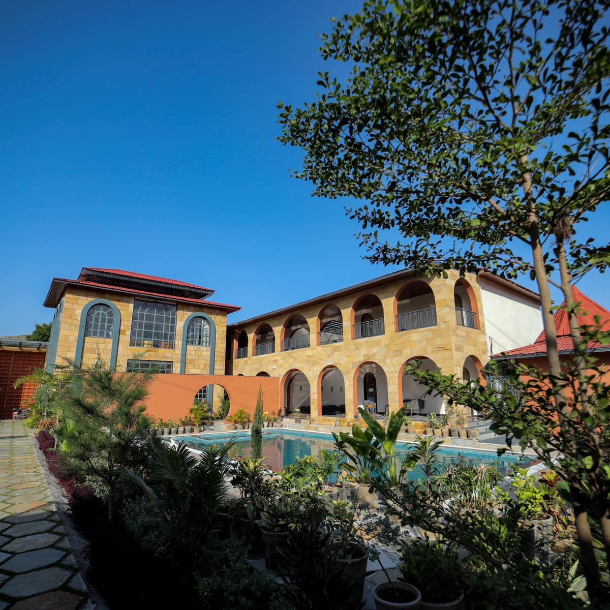 Arched sandstone facade and courtyard pool at Nazaara Hills Retreat, Udaipur, framed by garden greenery