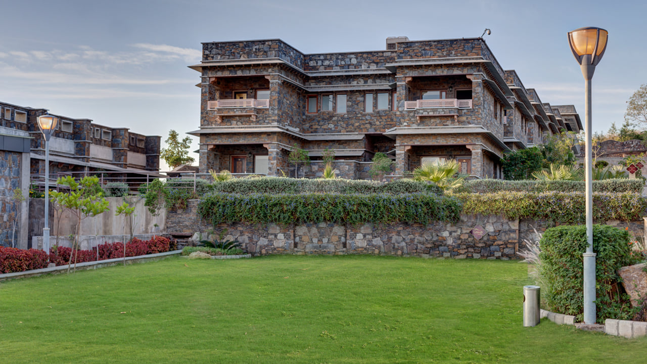 Garden lawn beside the stone buildings of Ramada by Wyndham Udaipur Resort and Spa