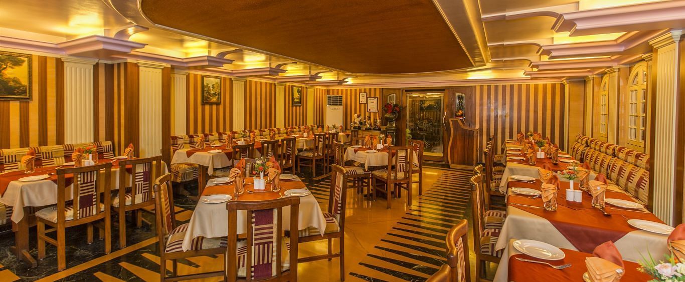 An image of a restaurant with several sets of chairs and table, and at one corner there is a reception desk - Hotel Pai Comforts JP Nagar Bangalore