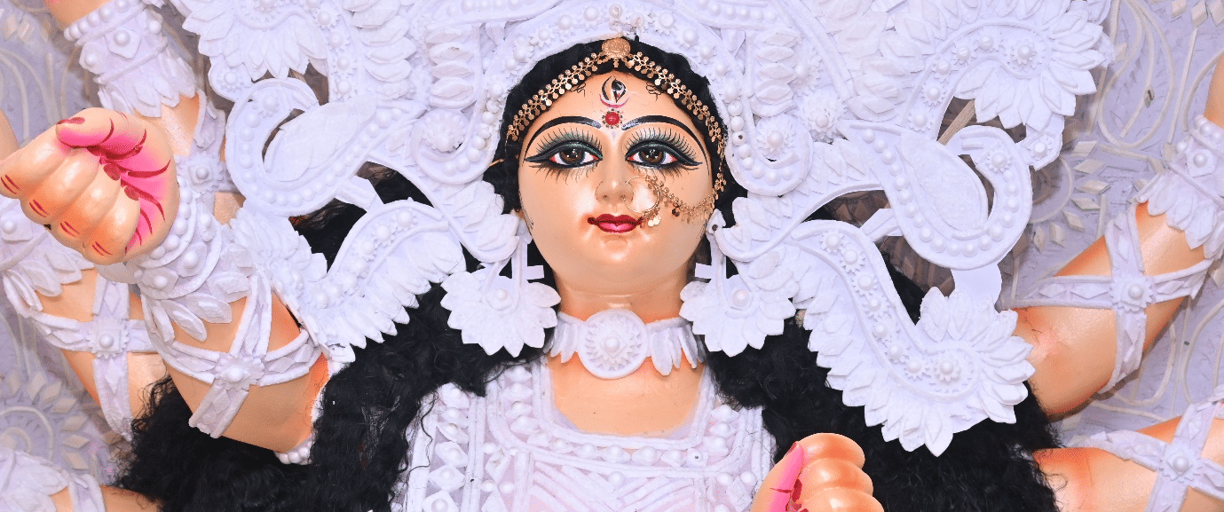A decorated Durga idol with a large white ornamental backdrop, holding lotus flowers in both hands.