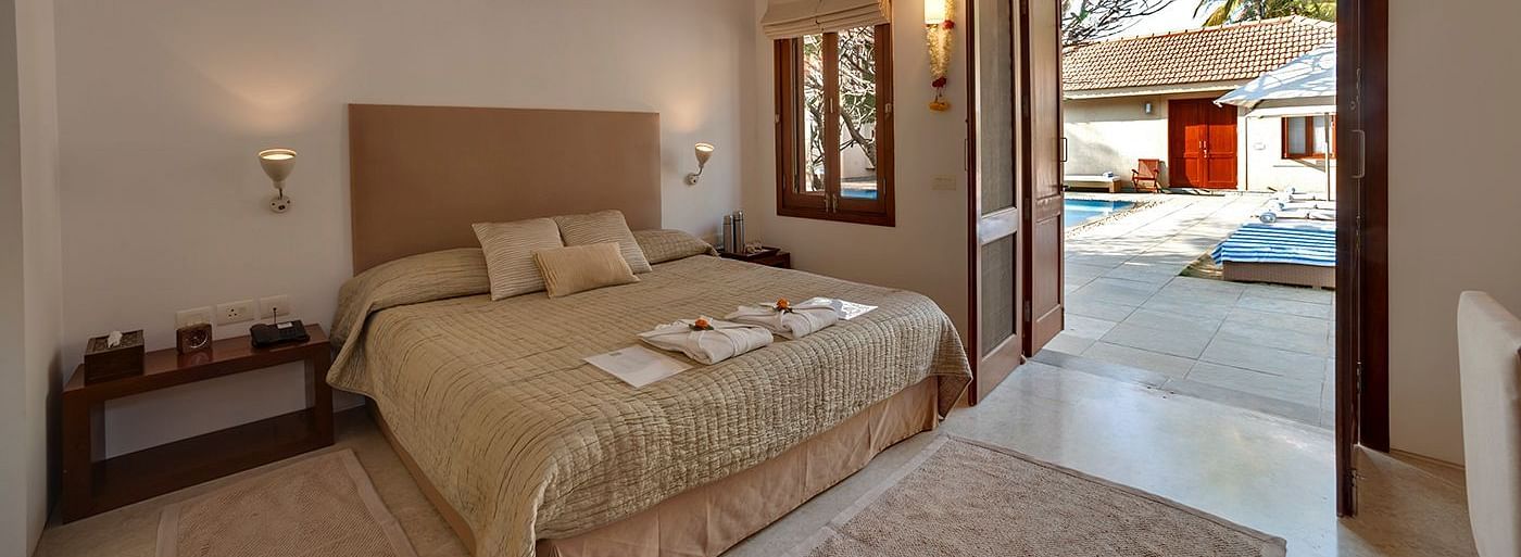 Neatly arranged bed with cushions and a view of the pool outside - Shreyas Retreat