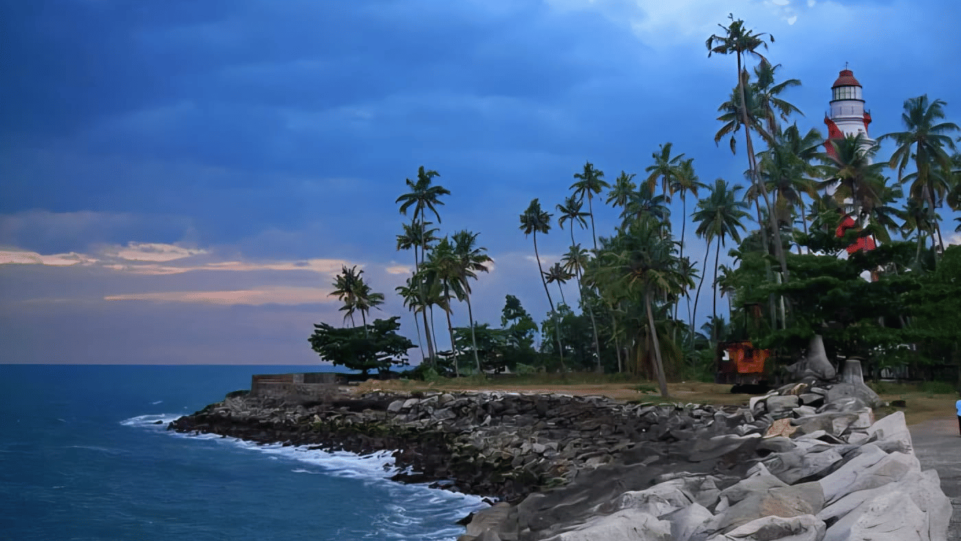 A rocky beach with crashing waves, silhouetted palm trees, and a distant lighthouse against a blue dusk sky.