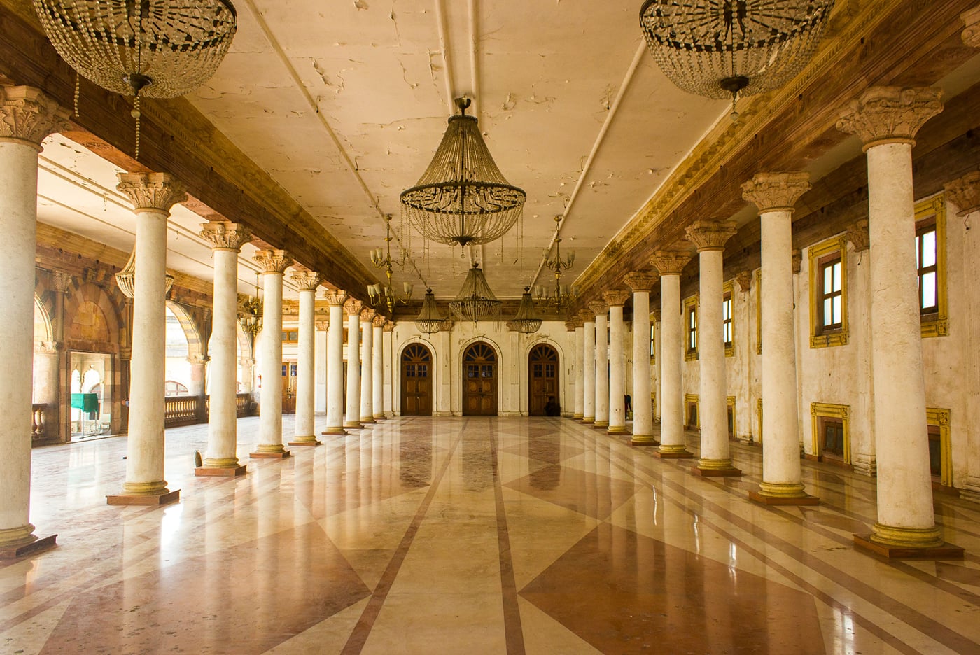 Long colonnaded hall inside Rajwada Palace in Indore with white pillars, chandeliers and a polished stone floor