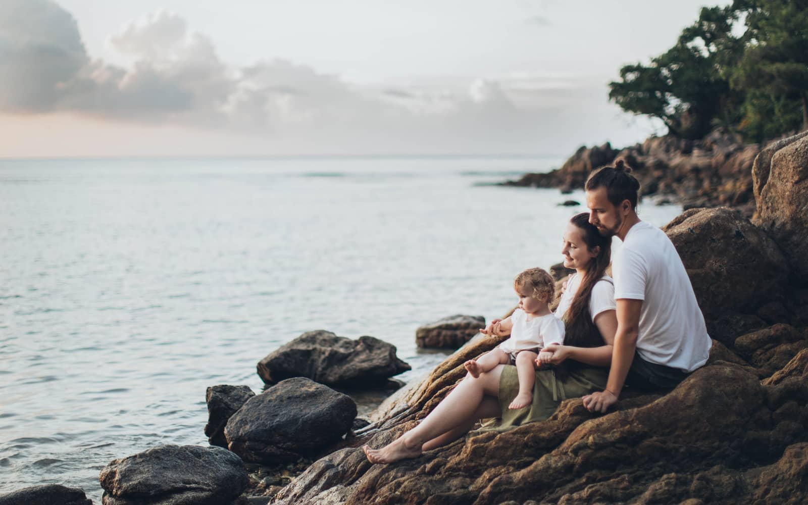 A family sitting together on the rocks at dusk, looking out over calm water