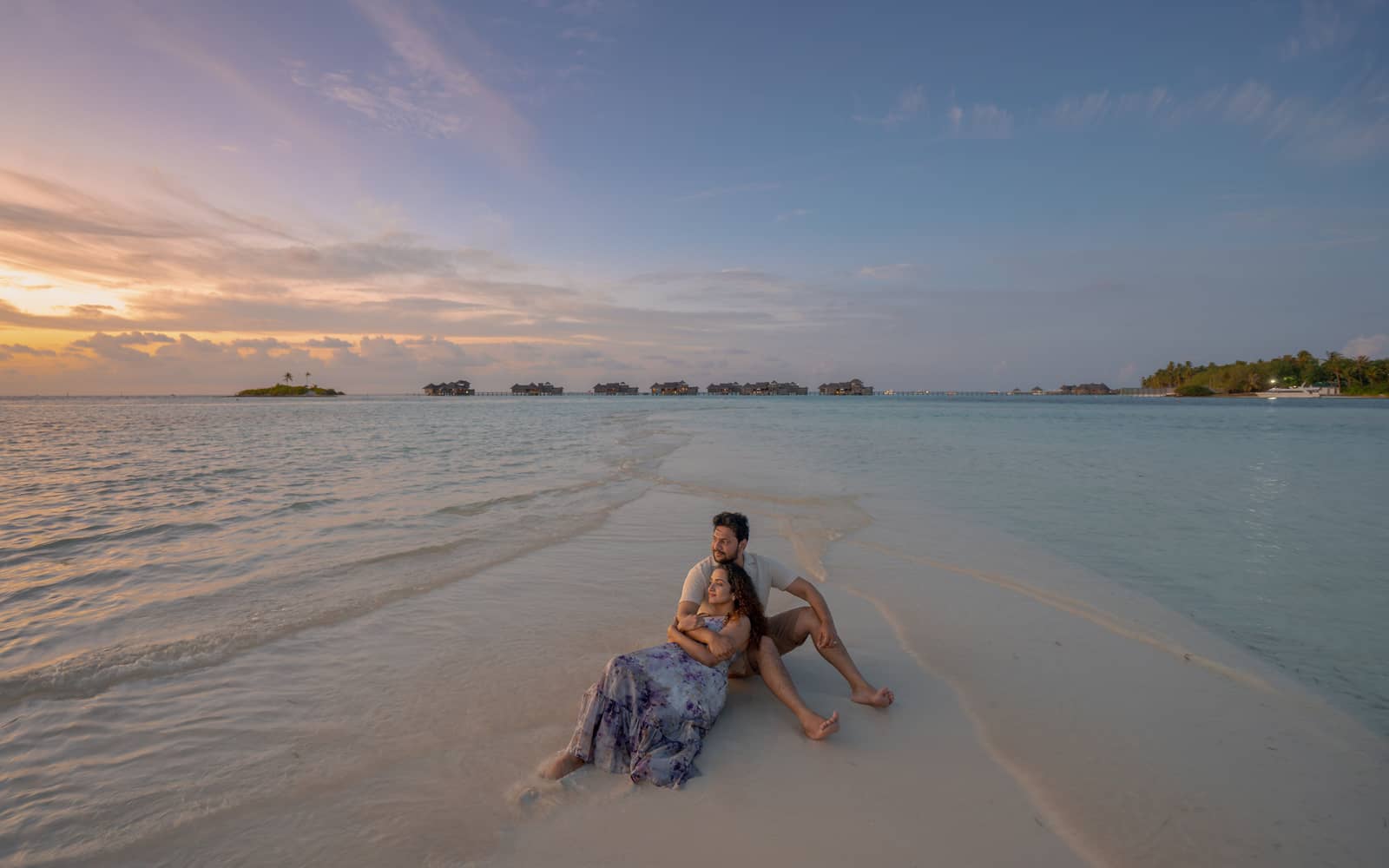 A couple resting on a sandbar at sunset, the shallows running out towards the horizon
