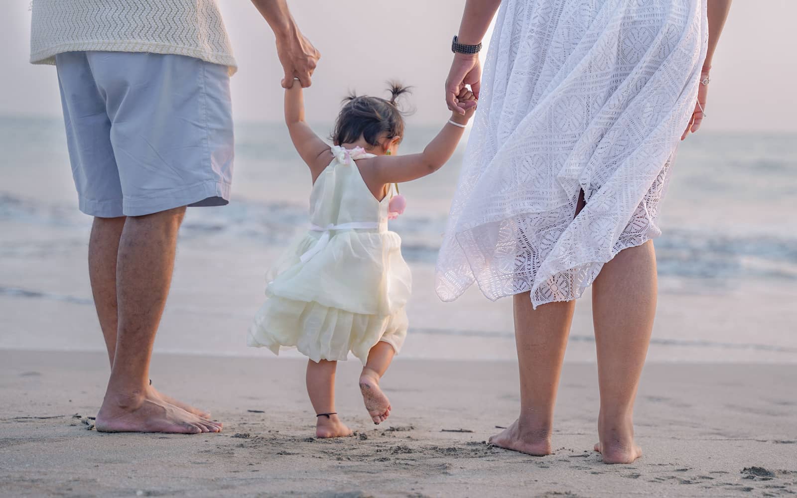 Parents walking hand in hand with a small child along the wet sand