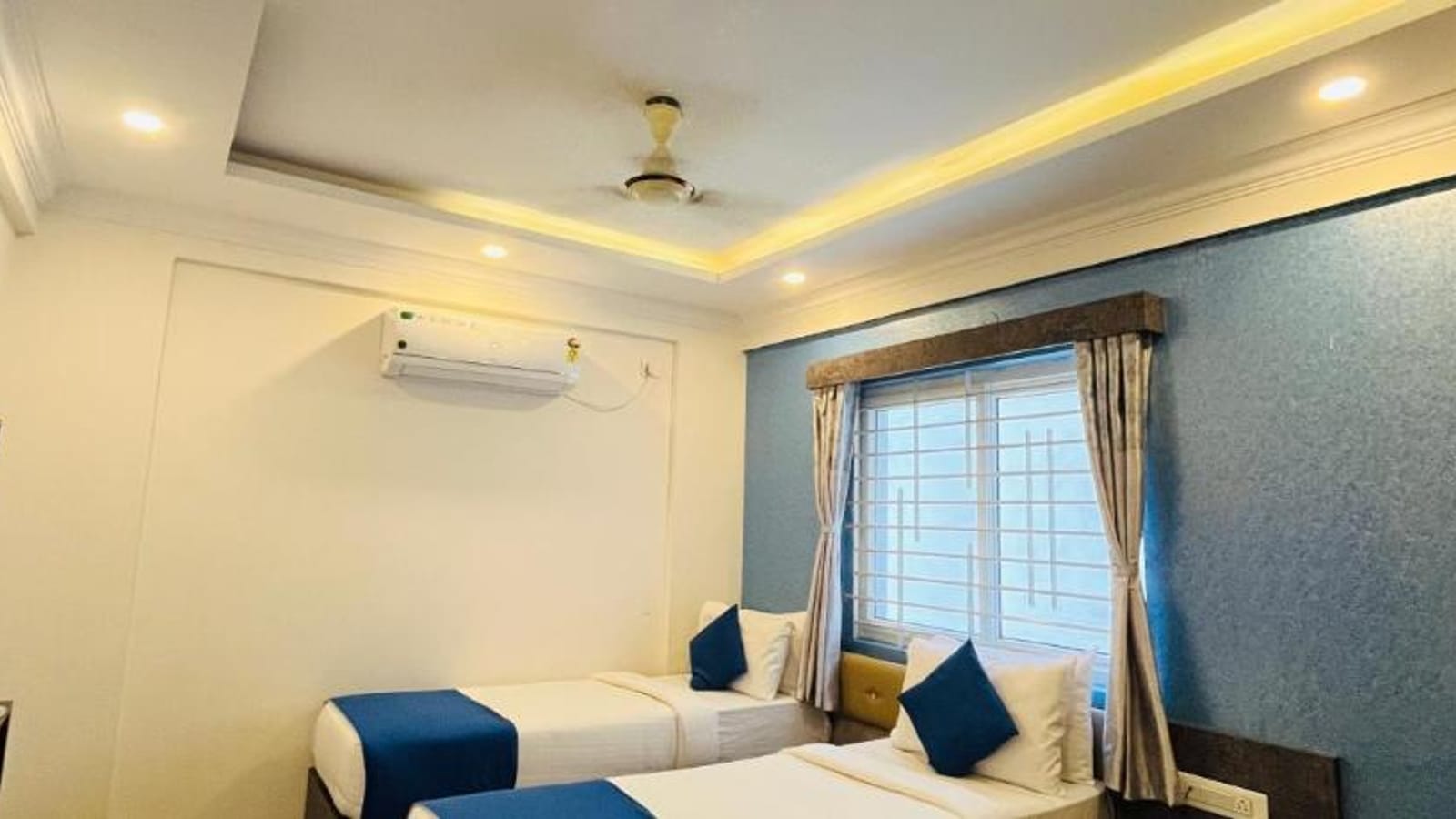 Standard AC Twin Room at Value Inn, Bangalore Airport with 2 single beds, a wall mounted air conditioner, and warm cove ceiling lighting