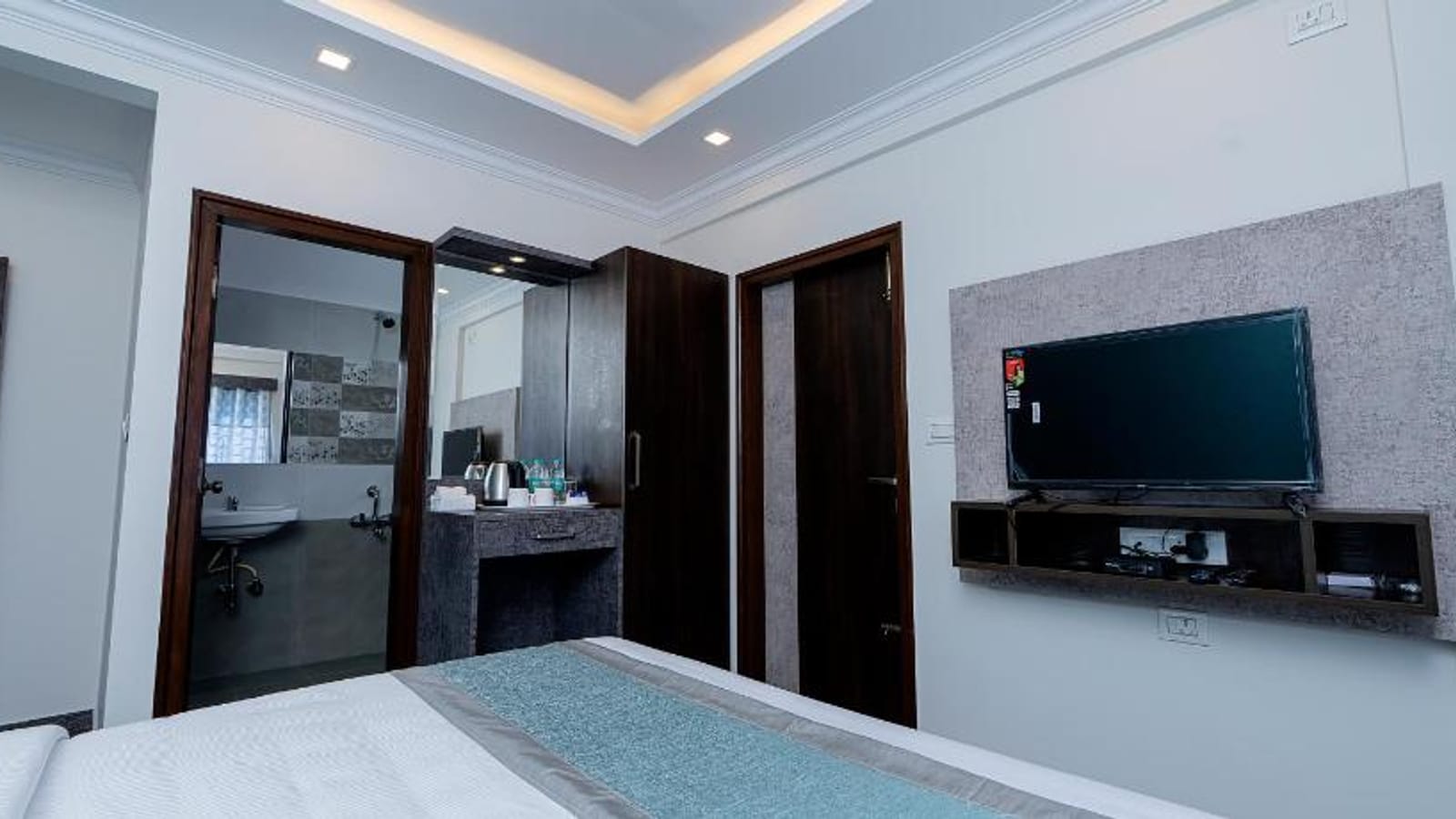 Wall mounted TV, dressing mirror, and bathroom entrance in the Standard Non-AC Room at Value Inn, Bangalore Airport with wooden doors