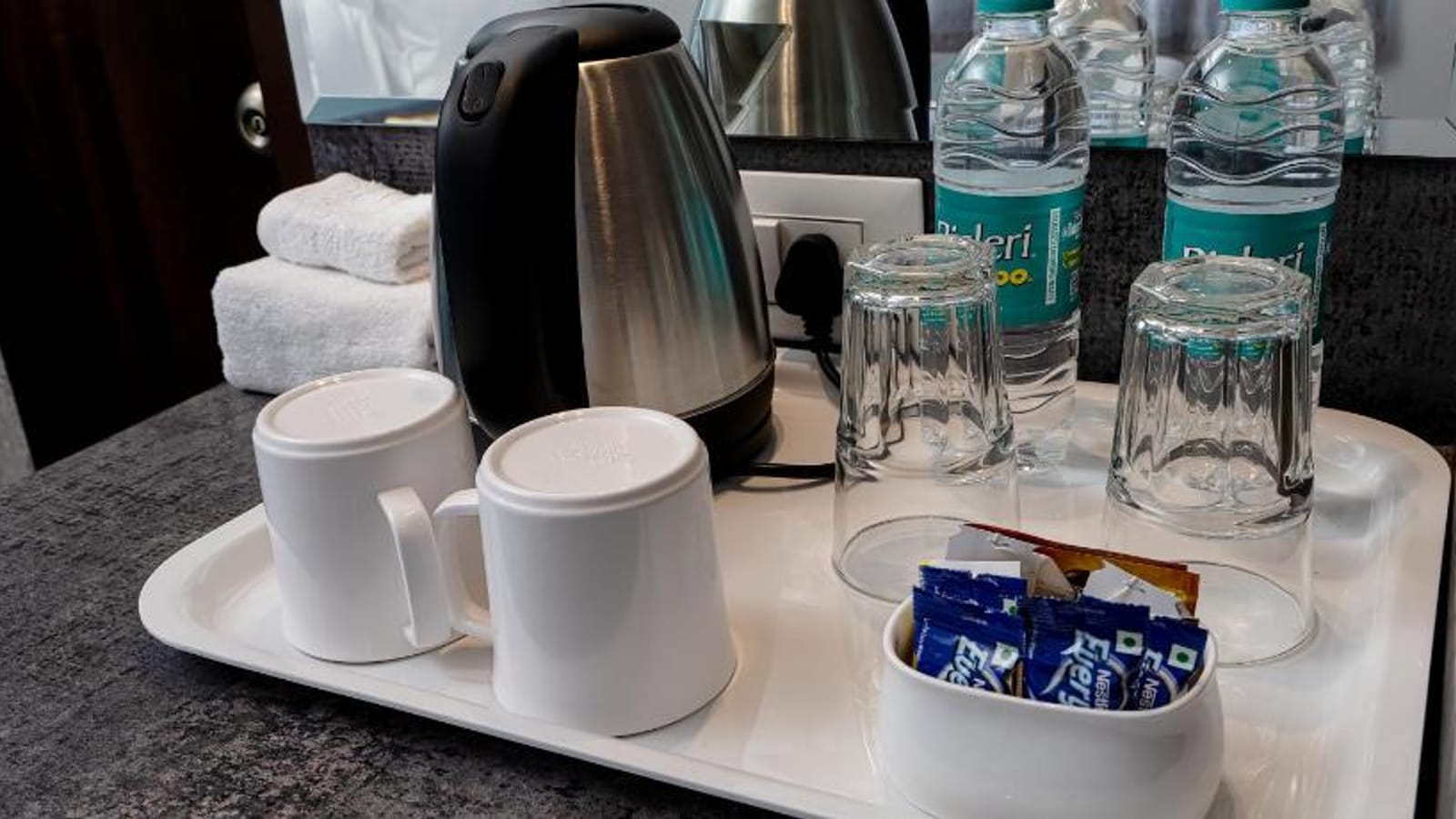 In room refreshment tray at Value Inn, Bangalore Airport with an electric kettle, cups, glasses, biscuit sachets, and mineral water bottles