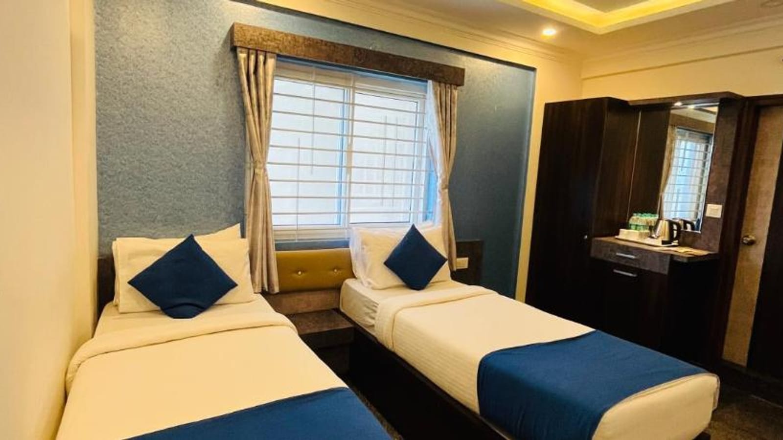 Standard Twin Non-AC Room at Value Inn, Bangalore Airport with 2 single beds, blue runners and cushions, a bright window, and a mirror unit