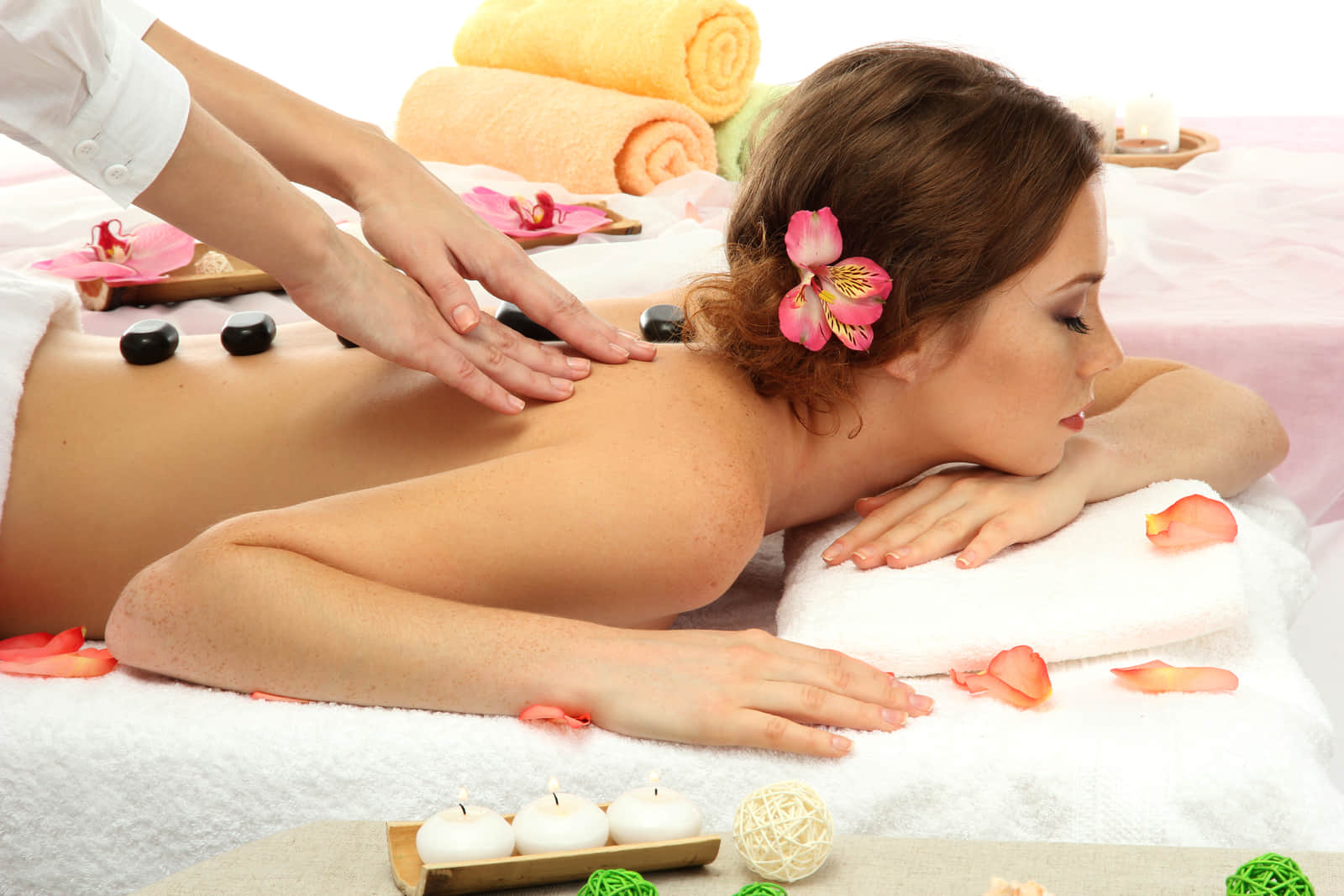 A guest having a hot stone back massage, rolled towels and flowers beside the table