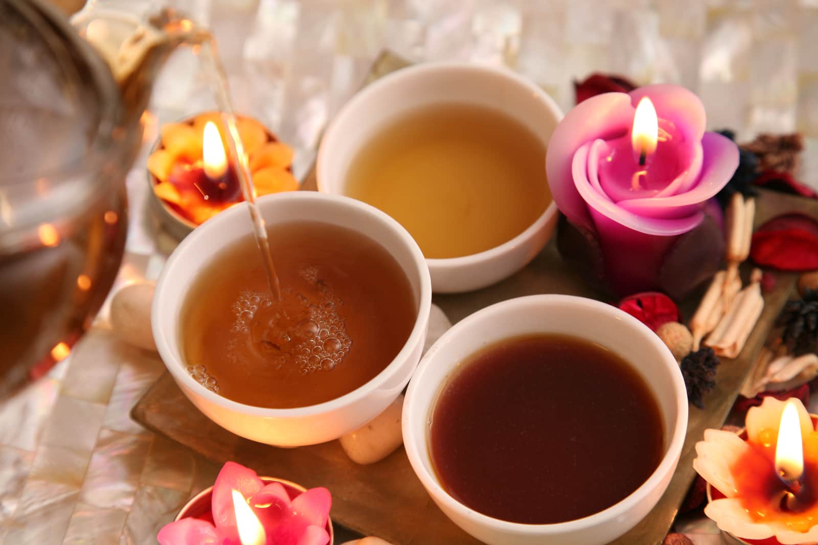 Bowls of Ayurvedic treatment oils, with lit candles and flowers set around them