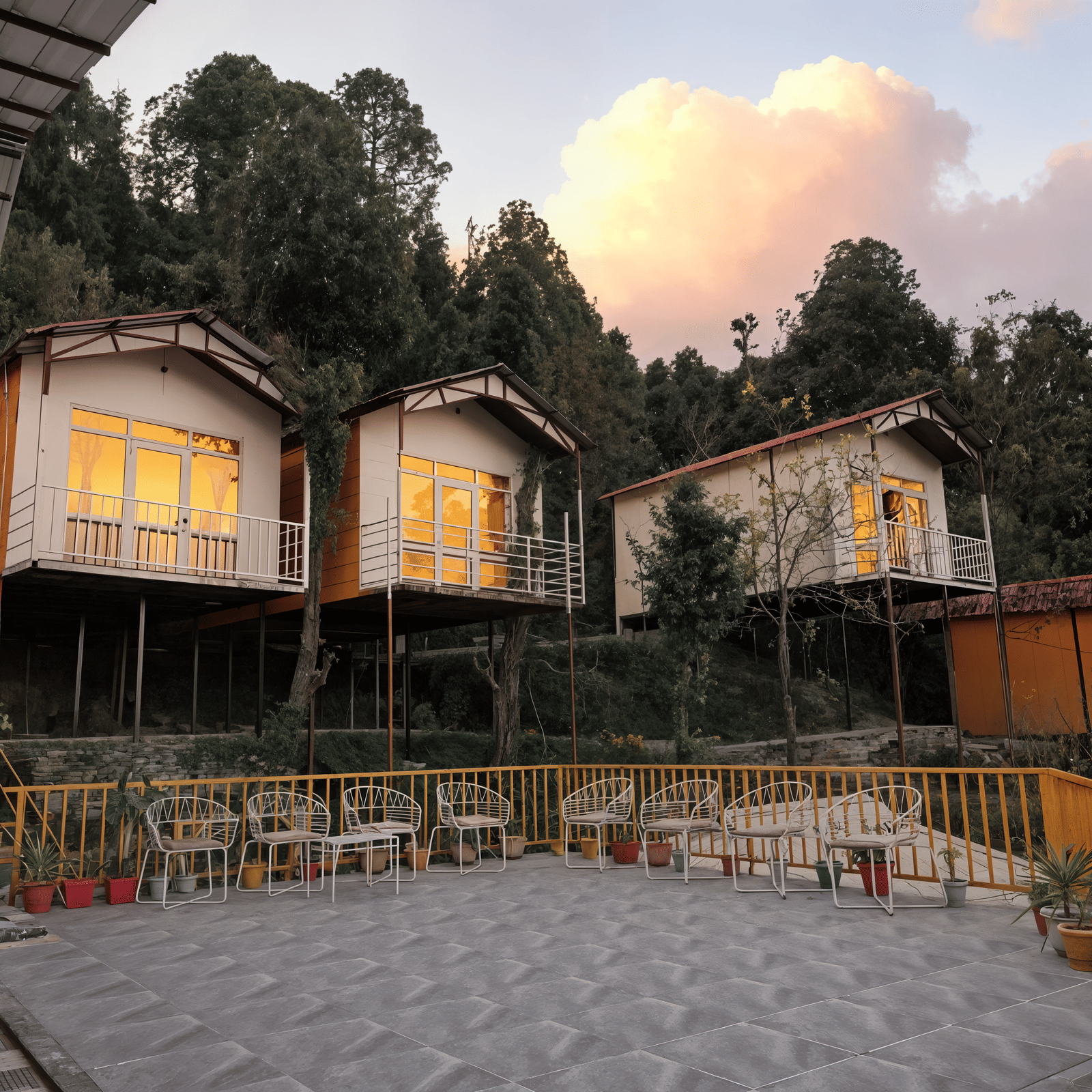 Wood-clad hillside cottages at Nazaara Nature Retreat lit warmly against a deep blue dusk sky over the Dalhousie hills