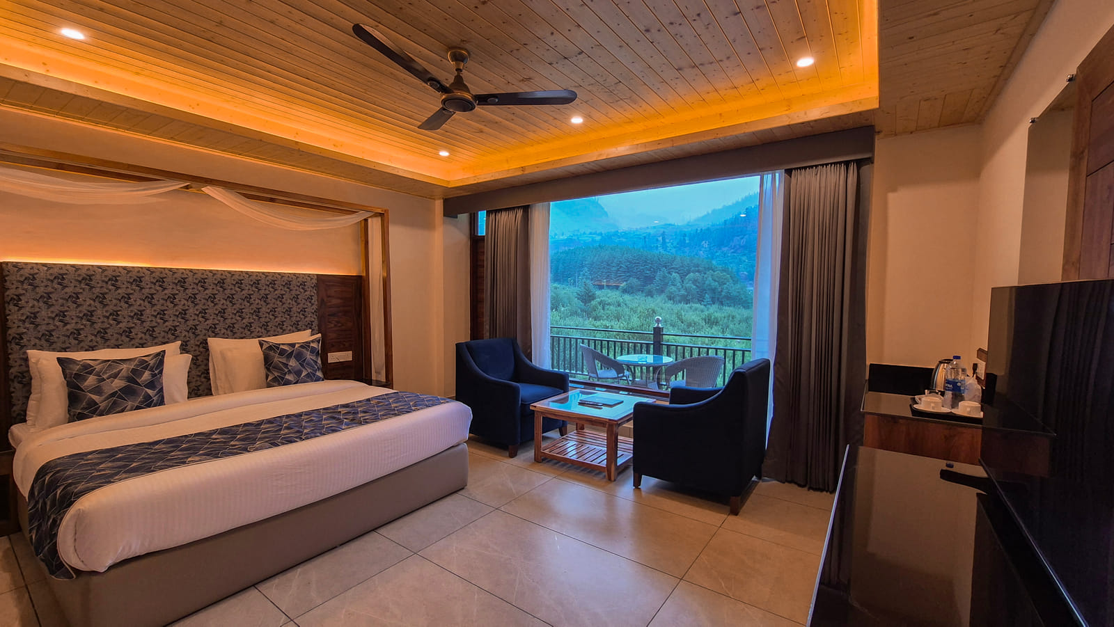 Bed beside the balcony door with a forest view in the Luxurious Room at Nazaara Luxe Retreat, Manali
