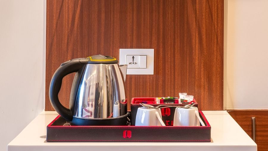 Mini-bar setup with snacks and beverages displayed beside tea and coffee amenities - Lords Eco Inn Shapar Rajkot