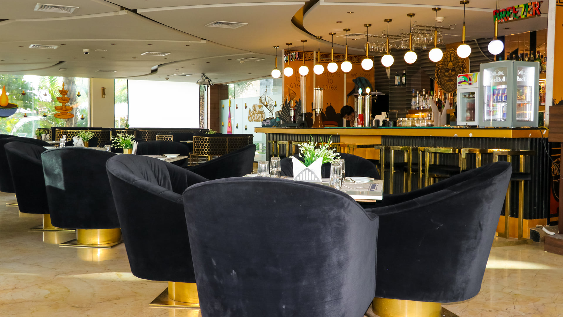 Black velvet armchairs at a set table in front of the gold-trimmed bar at Zeus restaurant