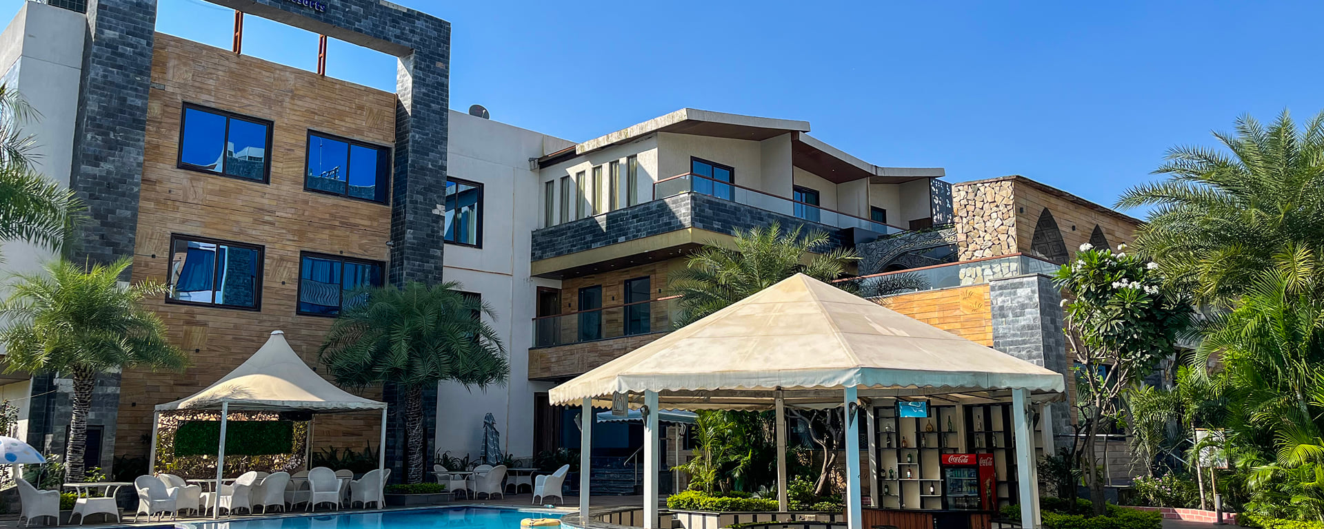 Hotel buildings and white gazebos beside the swimming pool under a clear blue sky