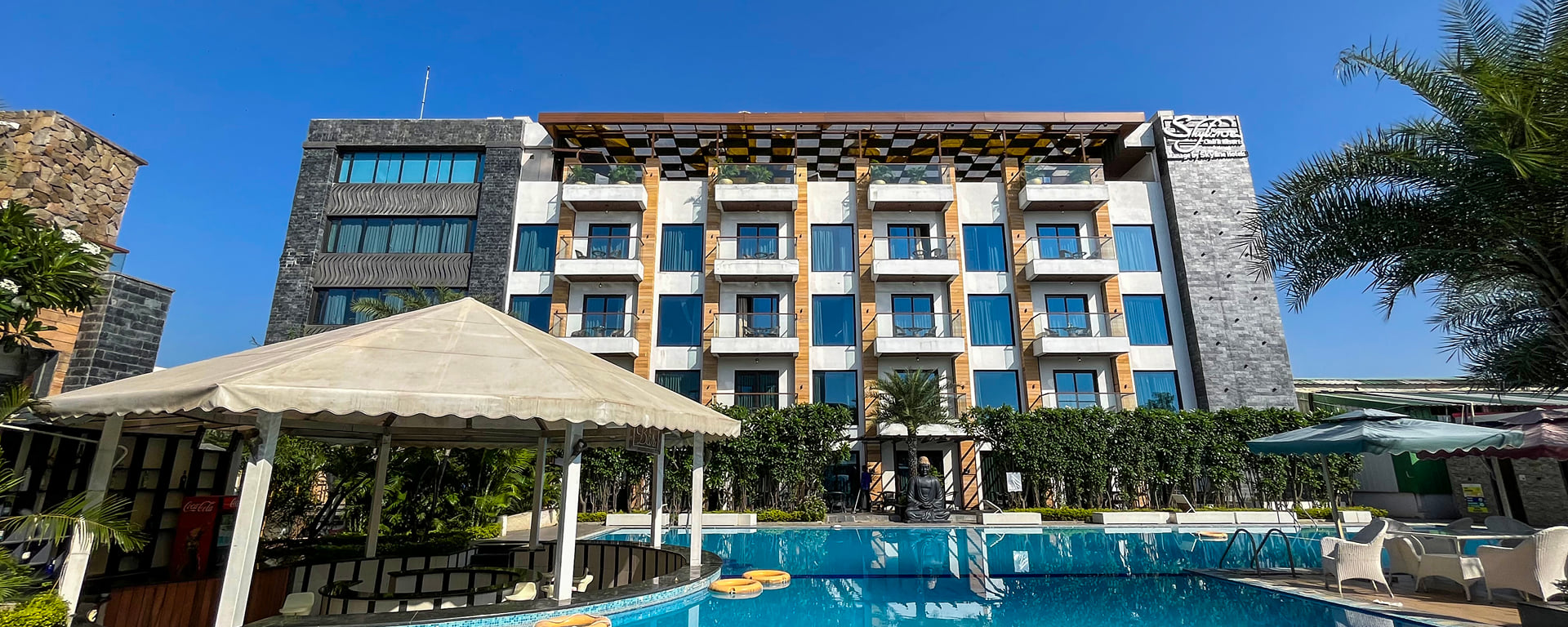 Swimming pool and white gazebo in front of the hotel building with blue-glass balconies
