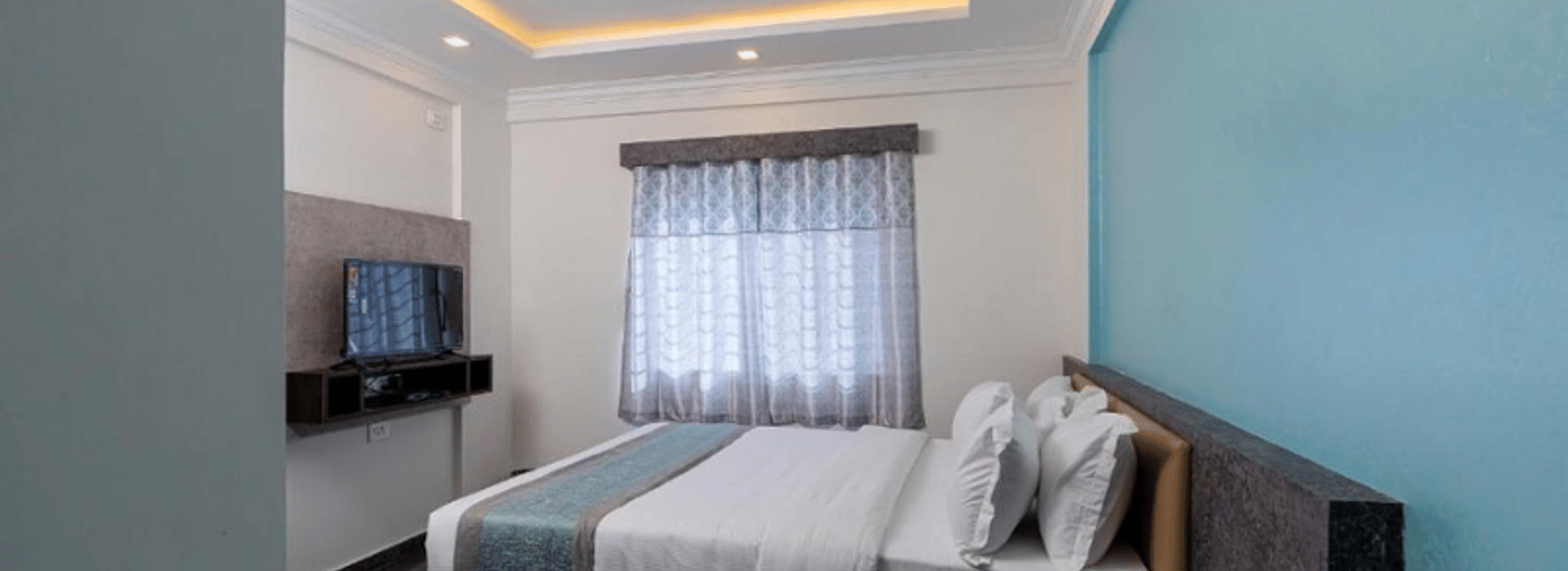 Standard AC Room at Value Inn, Bangalore Airport with a queen bed, teal feature wall, ceiling fan, cove lighting, and a curtained window