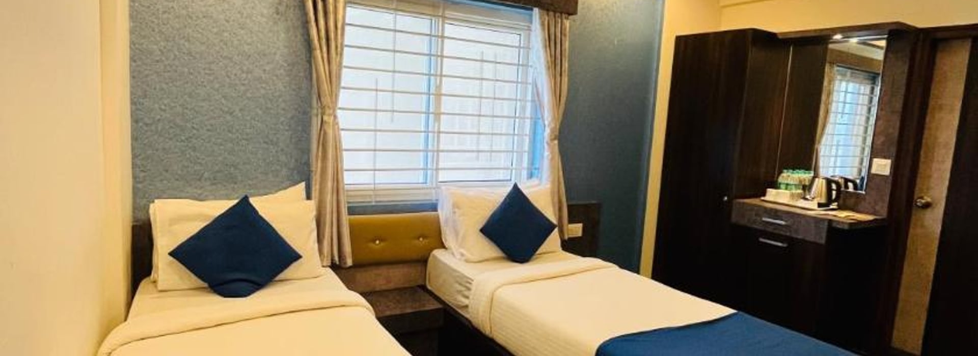 Standard Twin Non-AC Room at Value Inn, Bangalore Airport with 2 single beds, blue runners and cushions, a bright window, and a mirror unit