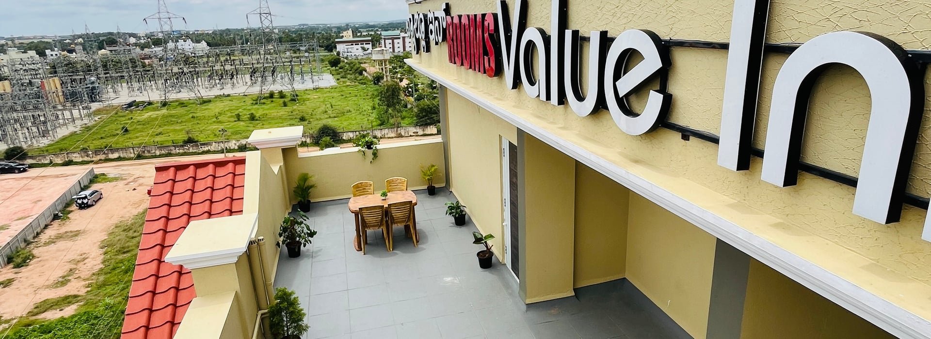 Rooftop terrace at Value Inn, Bangalore Airport with the hotel name board and open green views across the Yelahanka countryside nearby