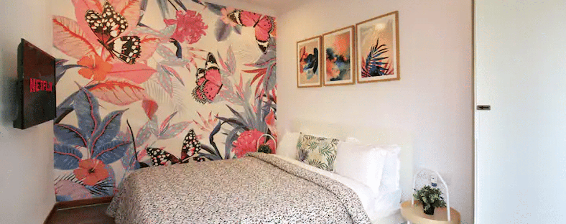 Bedroom at Wabi-Sabi, Juhu, with a floral butterfly mural, a matching printed duvet, a wall-mounted TV showing Netflix, and a white wardrobe.
