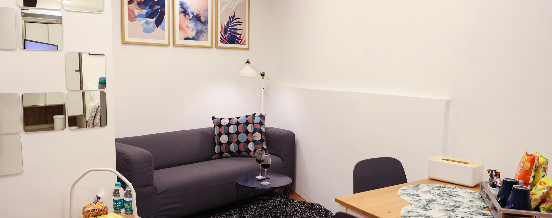 The Room 501 living room at Wabi-Sabi, Juhu with a grey sofa, patterned cushion, round coffee table, dining table with 2 chairs, and a fruit tray.